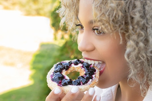 Healthy looking young woman taking a bite out of a sesame seed bagel with cream cheese and haskap berry preserve in an outdoor setting.