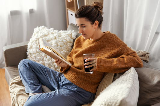 Woman in a cozy jumper reading a book on a sofa with a glass of Haskap juice