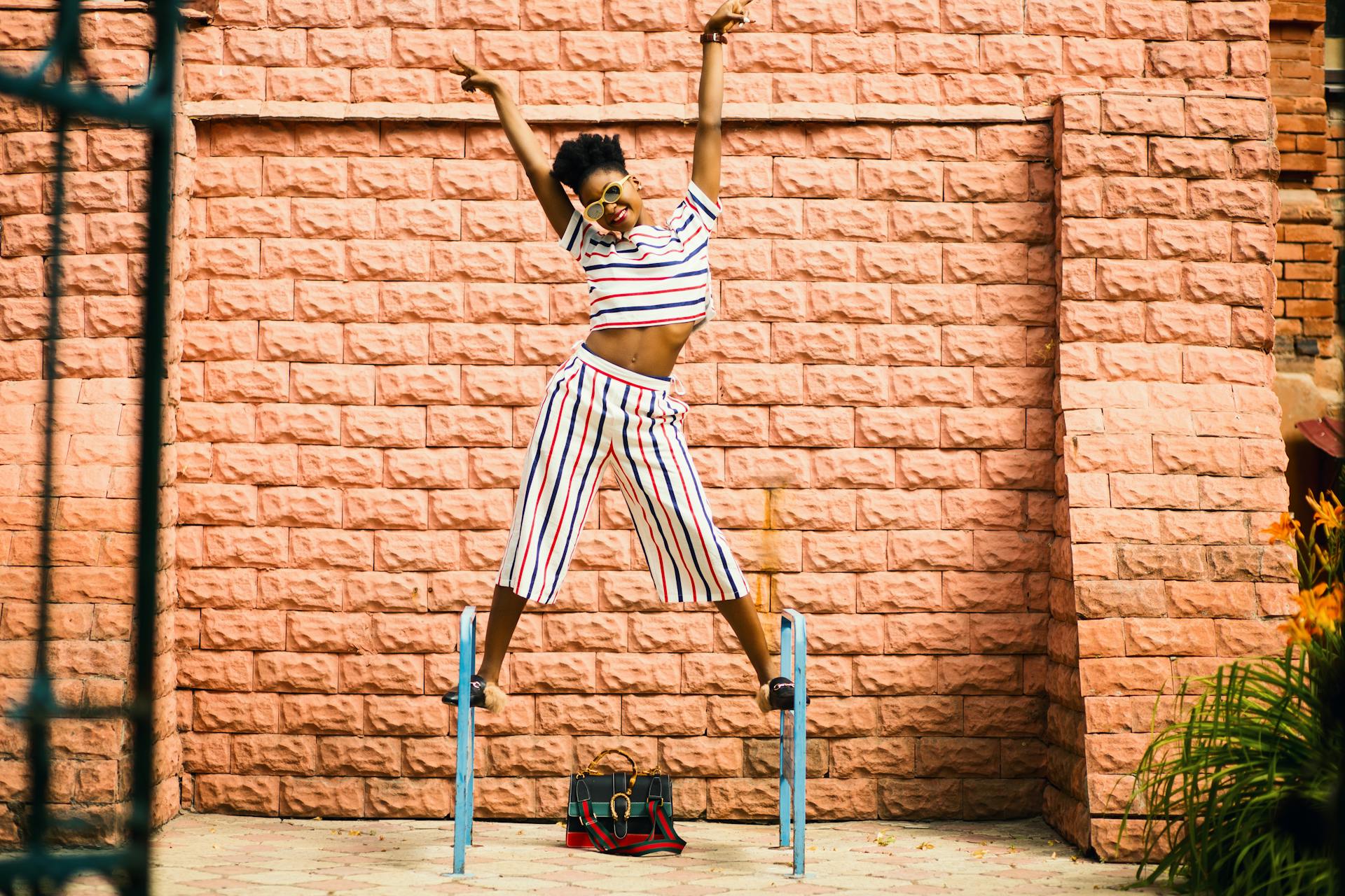 Woman balancing on supports outside with sunglasses and arms raised looking vibrant and victorious