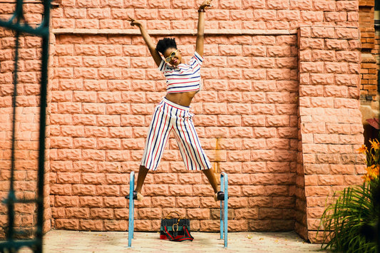 Woman balancing on supports outside with sunglasses and arms raised looking vibrant and victorious