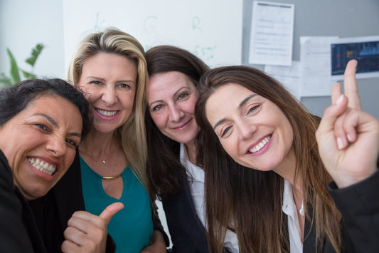 Smiling group of 4 middle aged women posing with thumbs up and peace sign