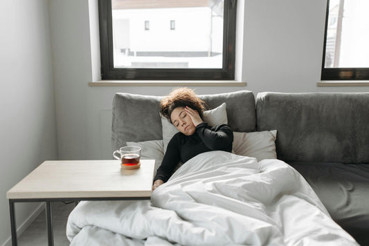 woman nursing a headache on the sofa with a duvet and a cup of tea.