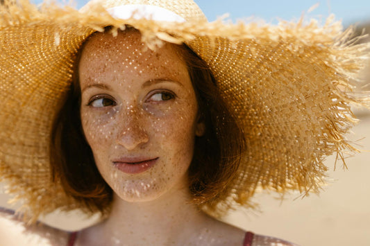 Woman protecting her skin from sun damage using a large straw hat on a beach.